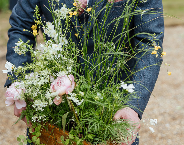 Suited man holding a loose garden-style bouquet of greenery and pale flowers