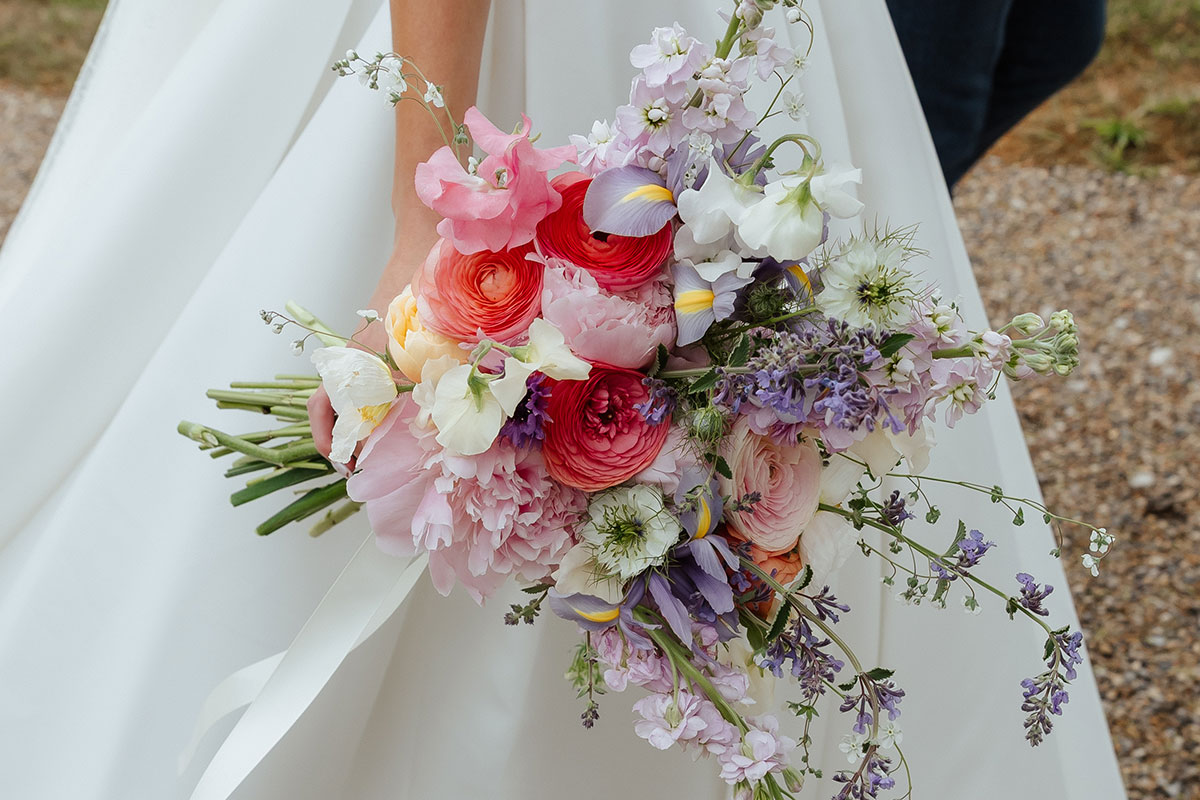 Bride holding a vibrant bouquet of peonies, ranunculus, sweet peas, and lavender