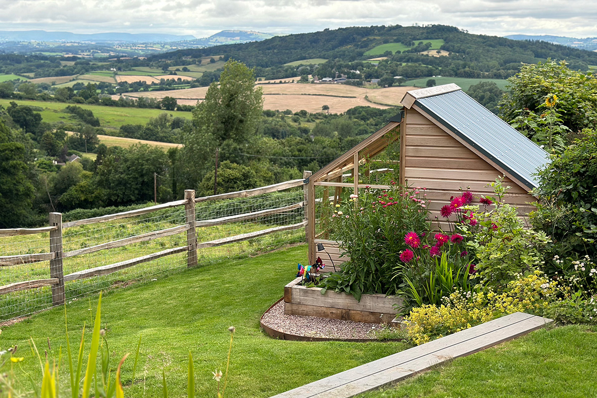 Small wooden garden shed with raised beds and colourful flowers overlooking countryside views in Mitchell Troy